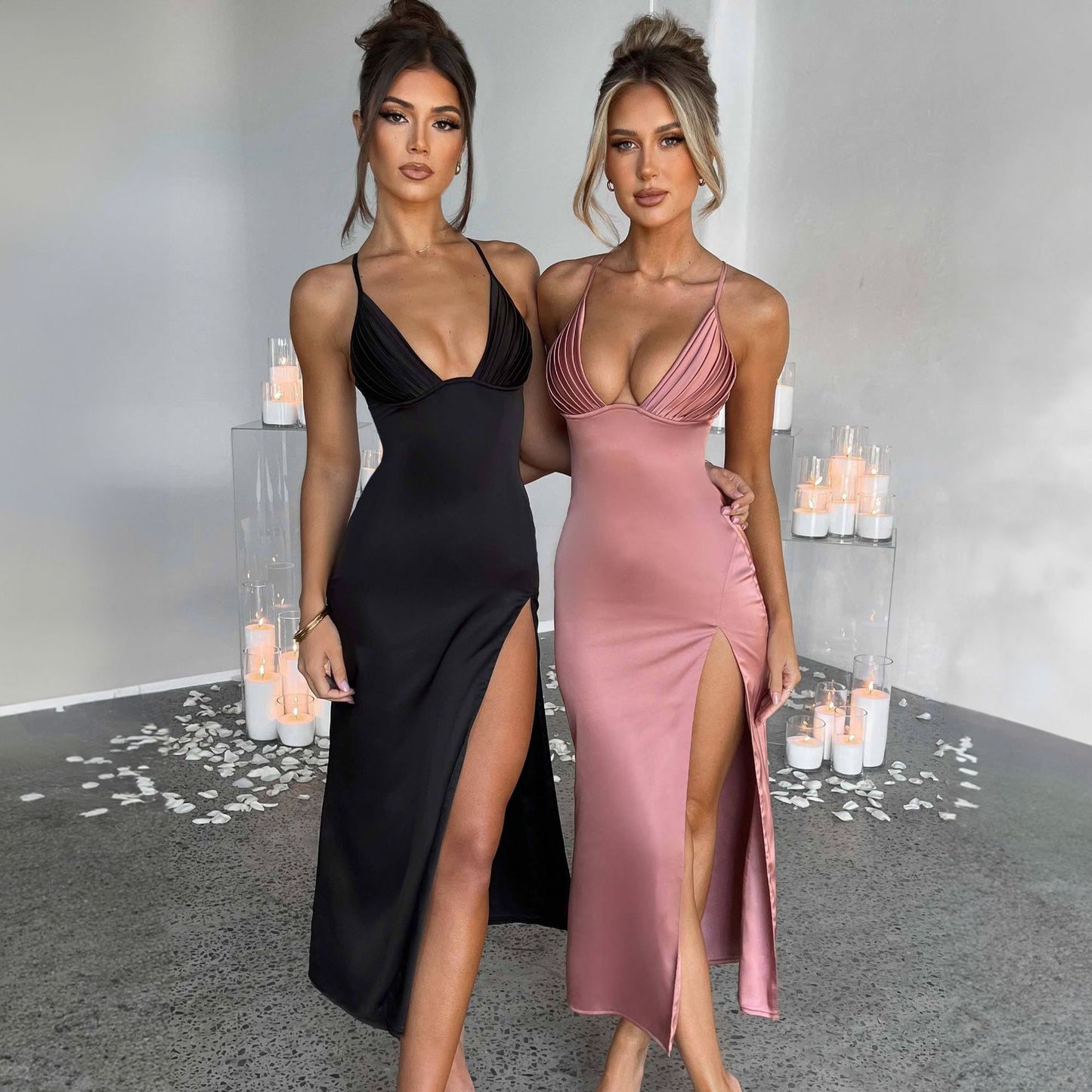 Two women in black and pink dresses standing in a decorated room with candles.